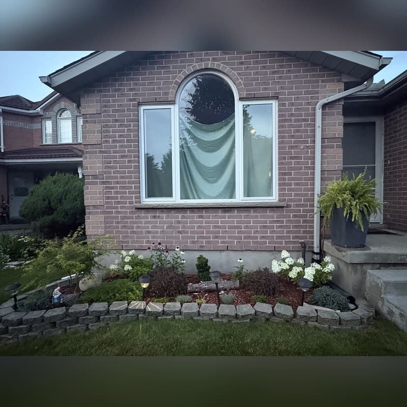 Brick house with an arched window and a stone-edged garden bed featuring white flowers.