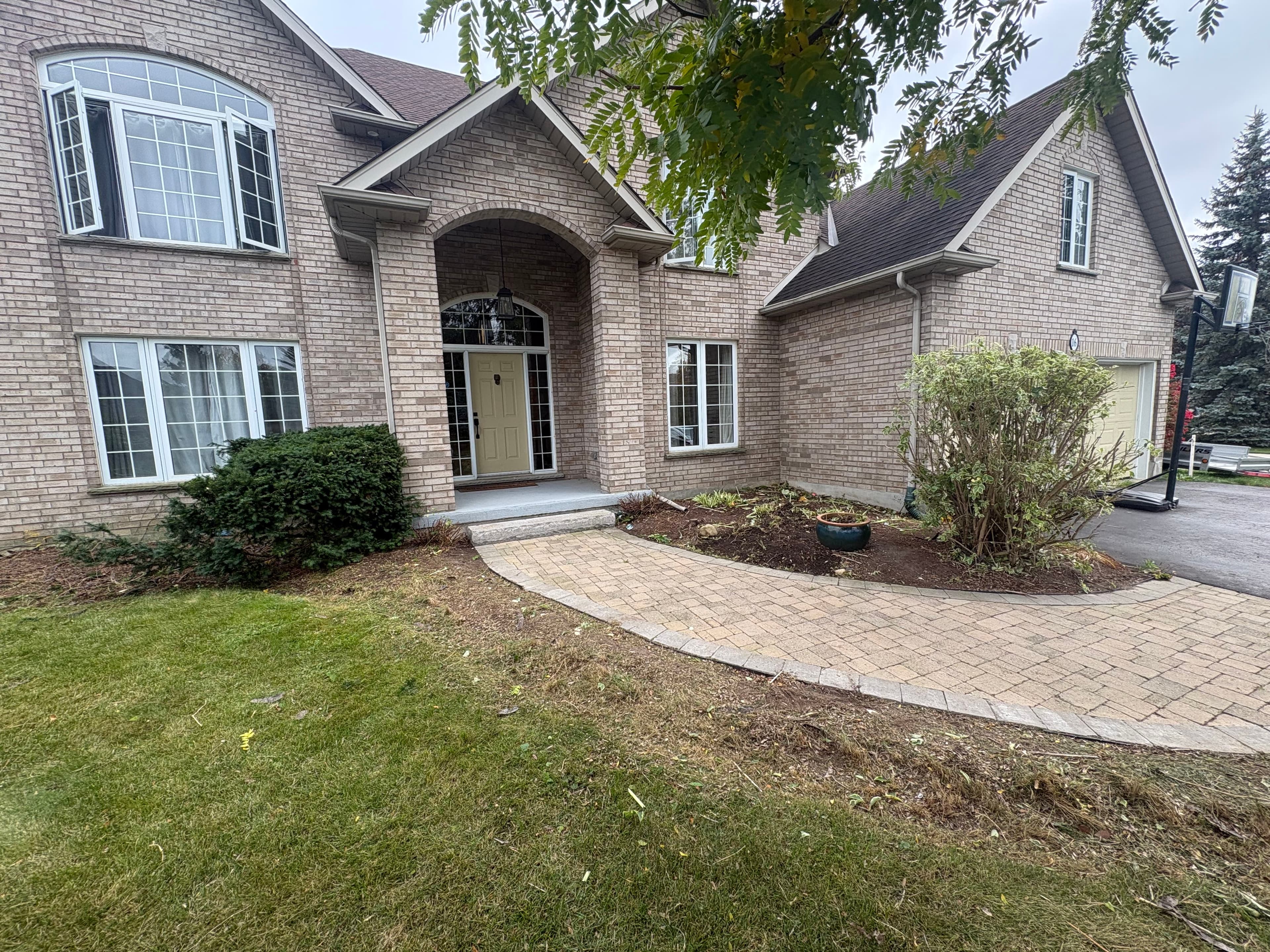 Large beige brick house with a curved stone walkway, arched entrance, and white-framed windows.