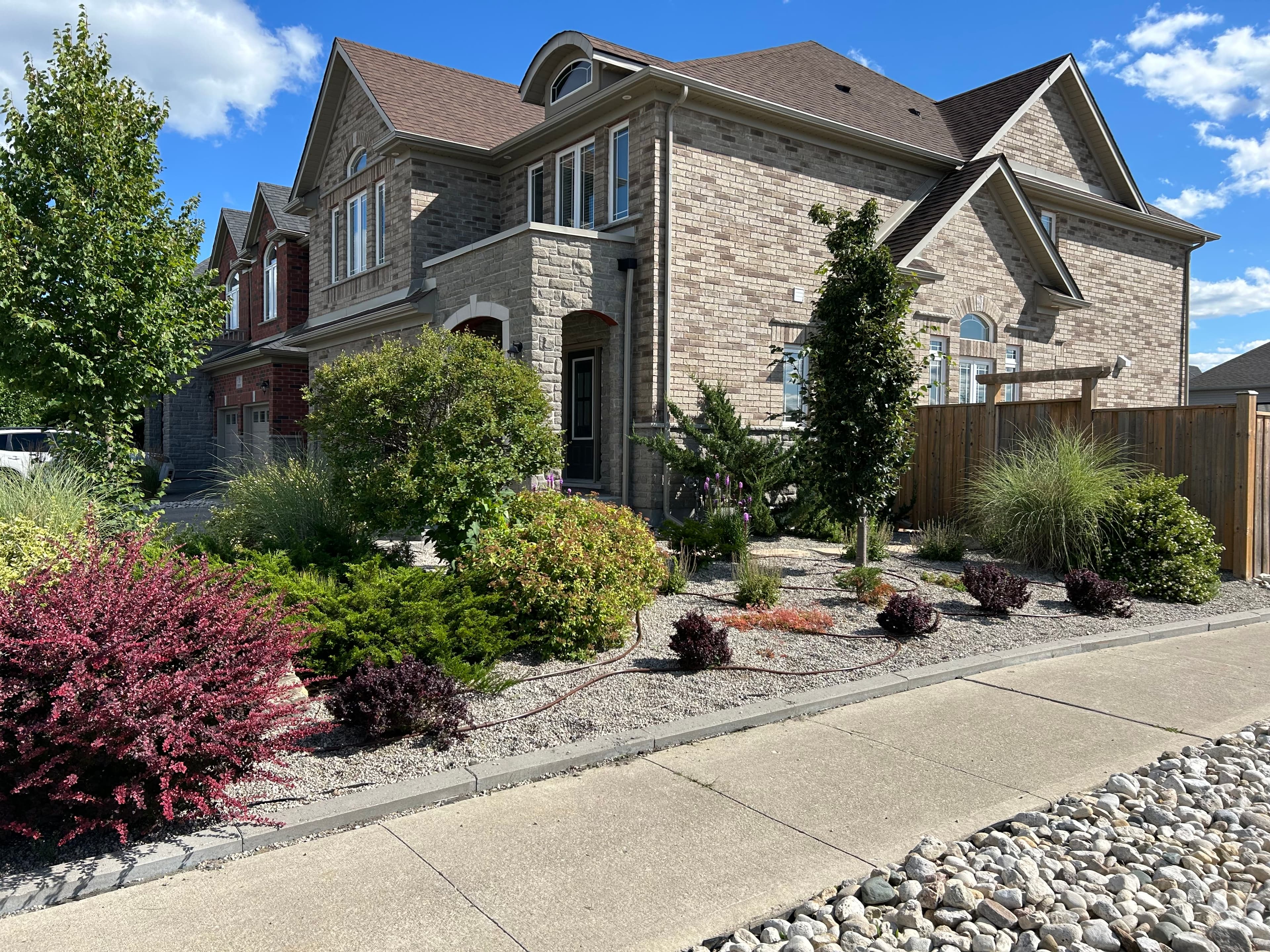 Large tan brick house with a landscaped yard featuring colorful shrubs and gravel mulch.